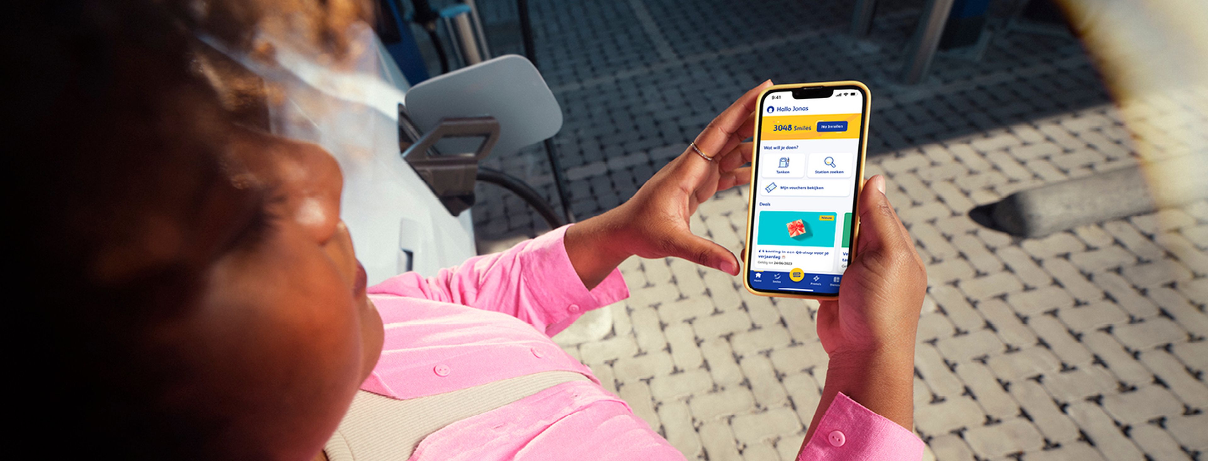 Une femme consulte l'application Q8 sur son téléphone dans une station-service Q8.