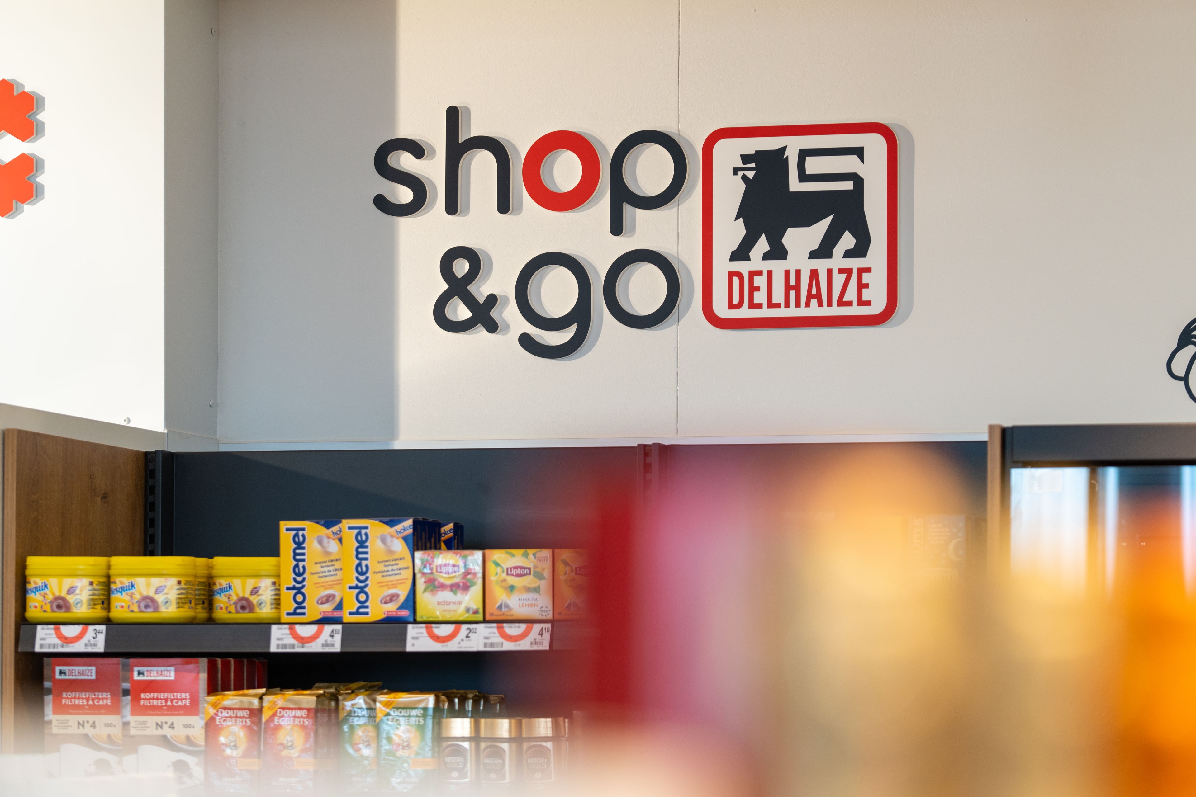 Delhaize shop&go logo boven winkelrekken met voedingsproducten