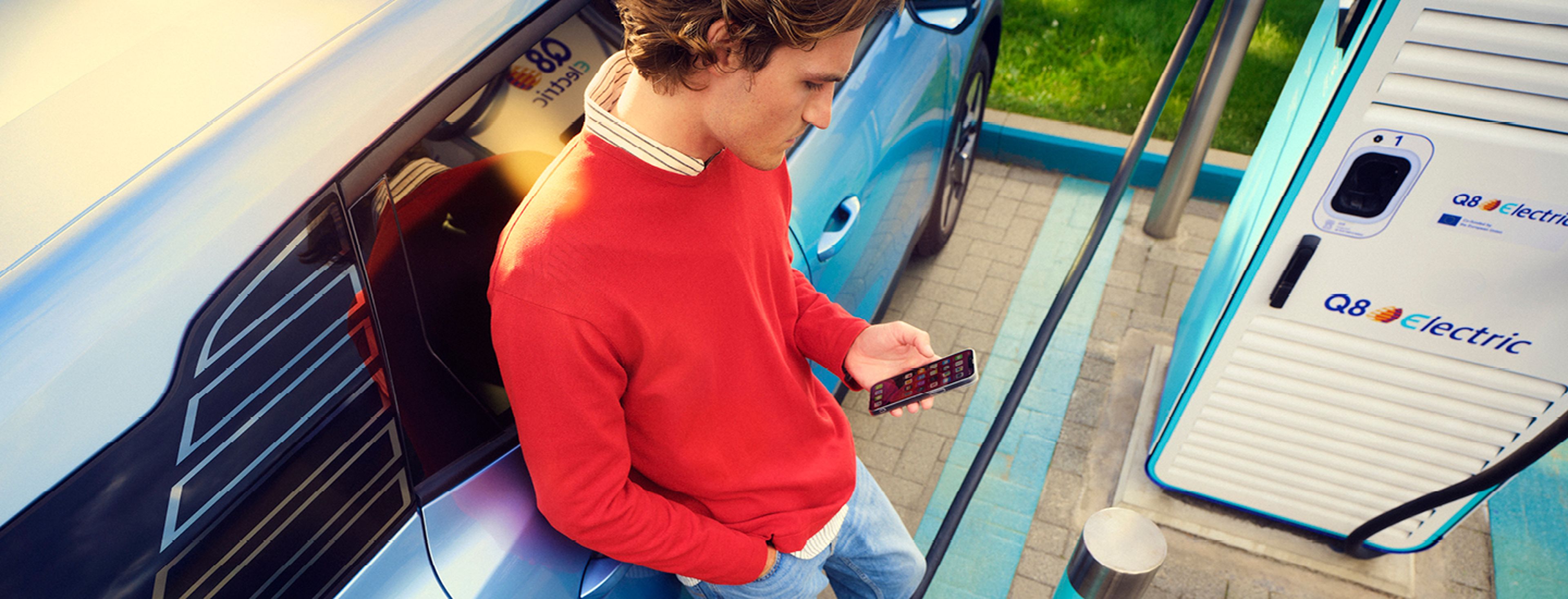 man heeft de Q8 electric app open en is aan het laden bij een Q8 laadstation