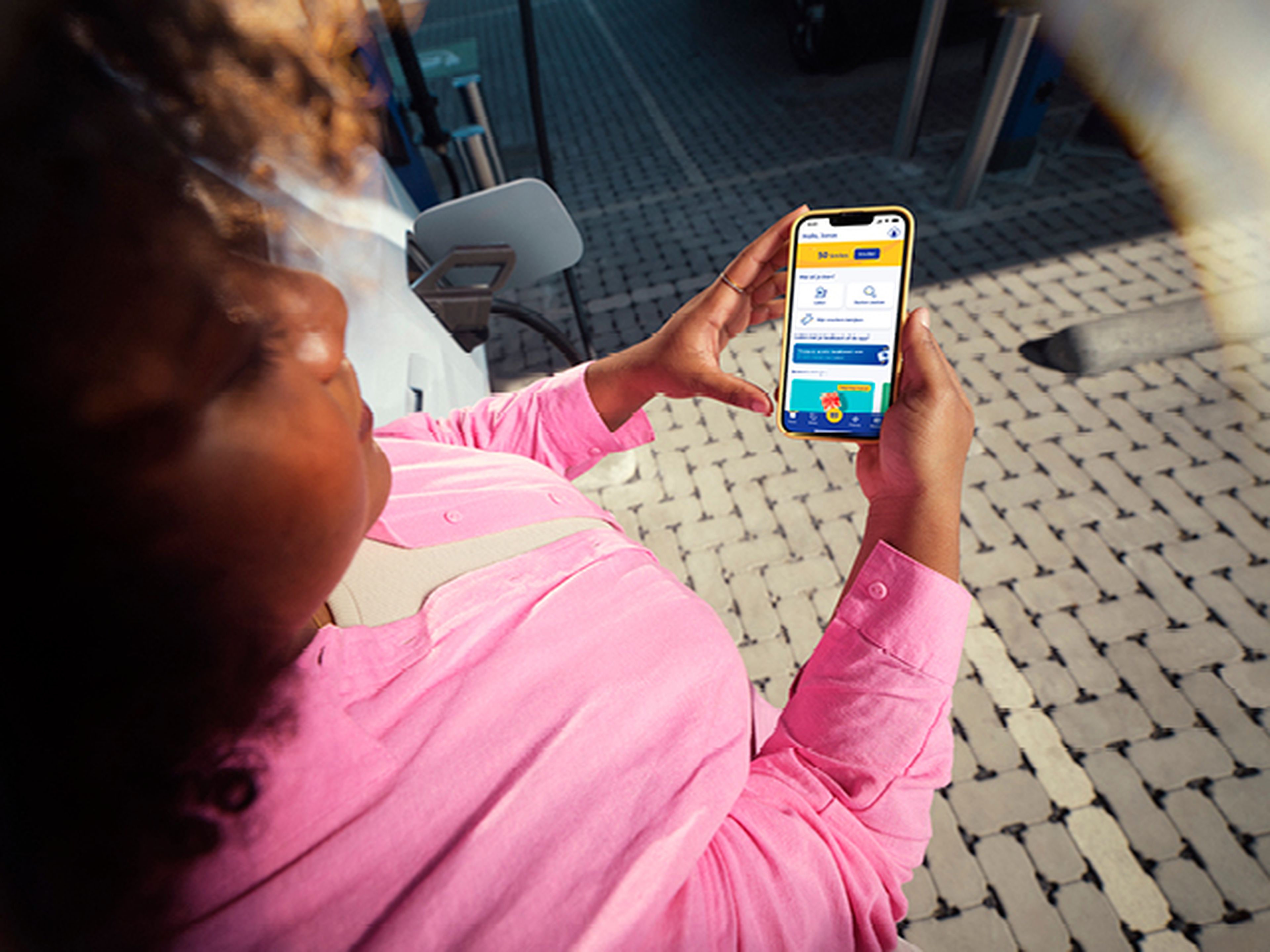 Vrouw kijkt op haar telefoon met Q8 electric app bij een Q8 laadstation.