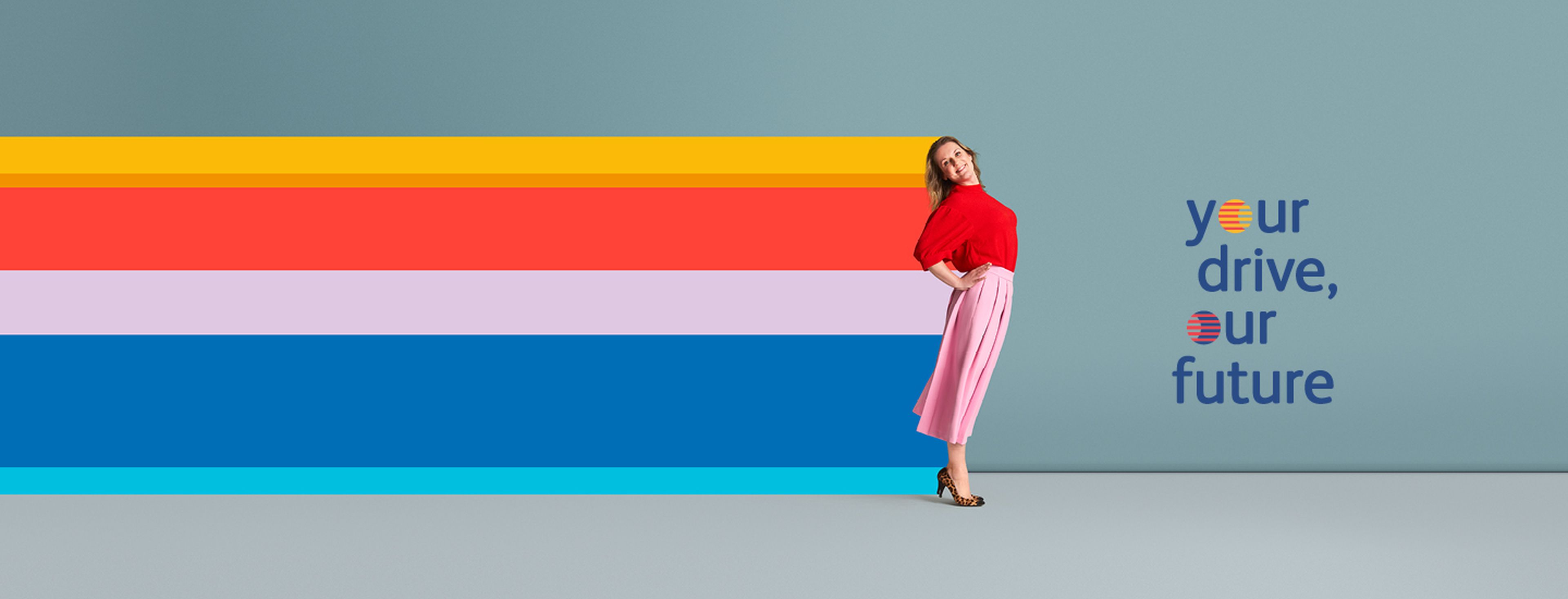 Een vrouw poseert vrolijk met een lichte buiging naar achteren tegen een effen blauwe achtergrond. Ze draagt een rode top, een roze geplooide rok tot halverwege de kuit en luipaardprint-hakken.
