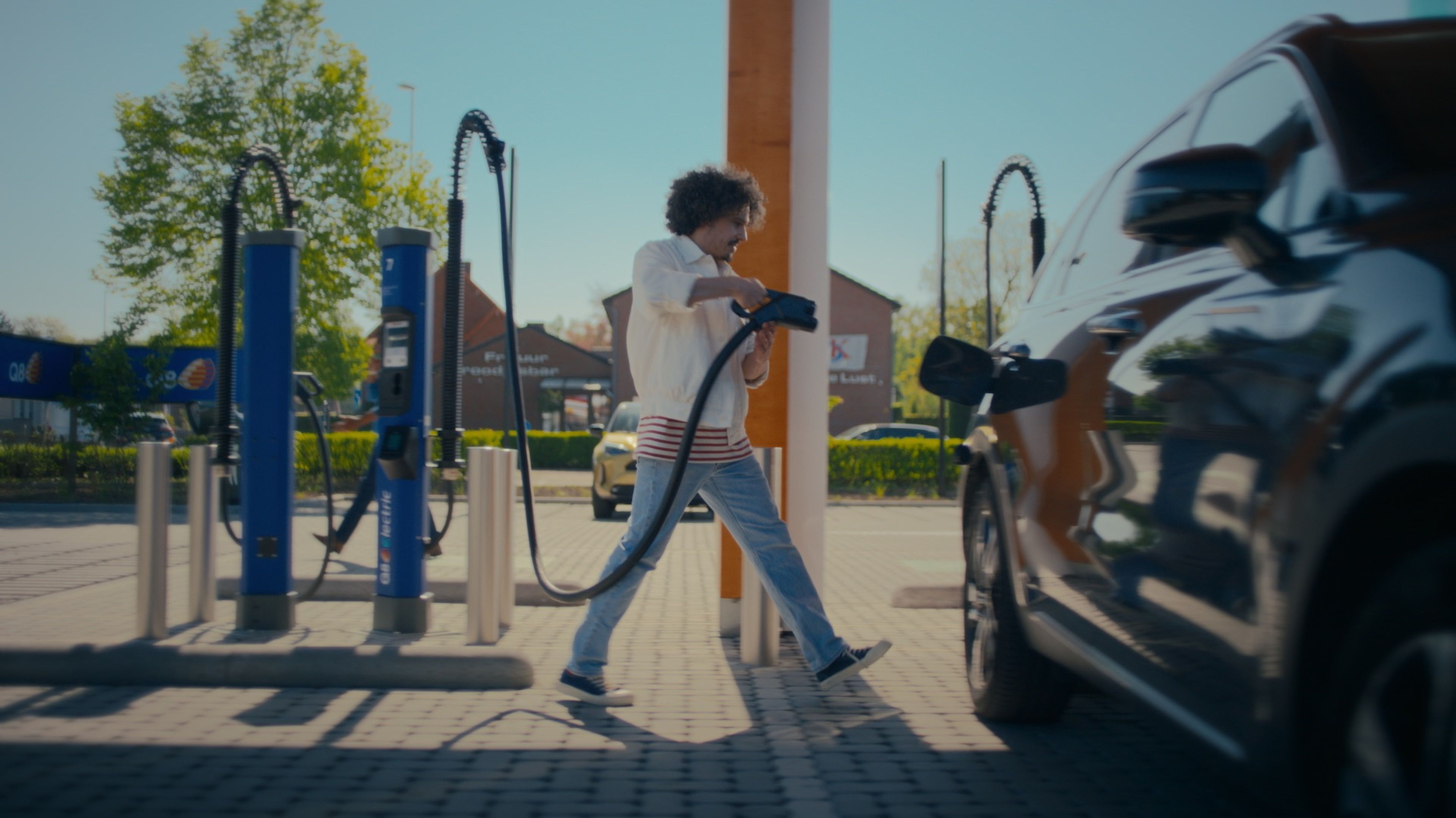 Woman looking at her phone with green screen near a Q8 charging station.