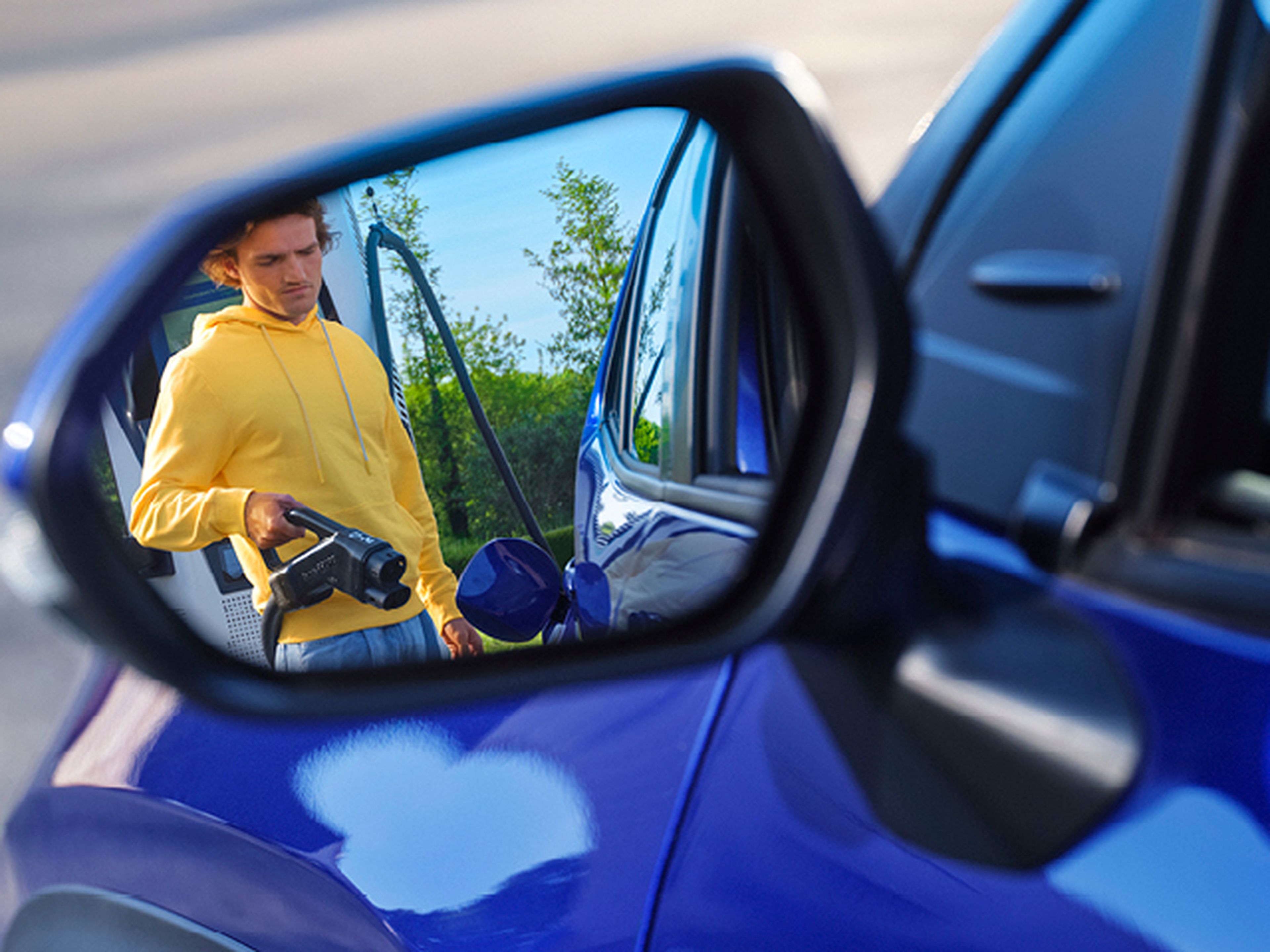 Een man in een gele trui steekt een snellader in zijn blauwe elektrische wagen bij een Q8 electric laadpaal.
