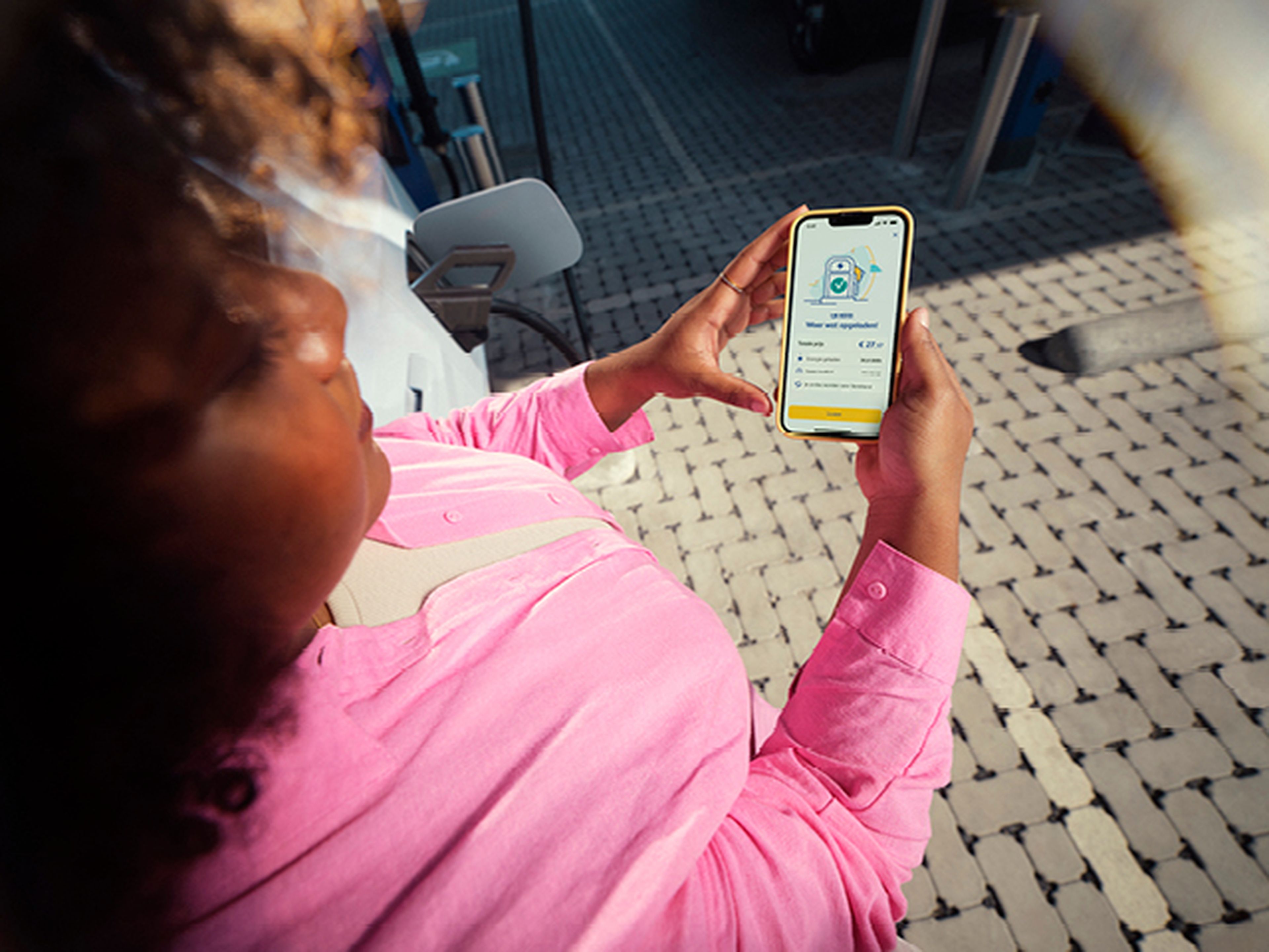 Vrouw kijkt op haar telefoon met de Q8 electric app bij een Q8 laadstation.