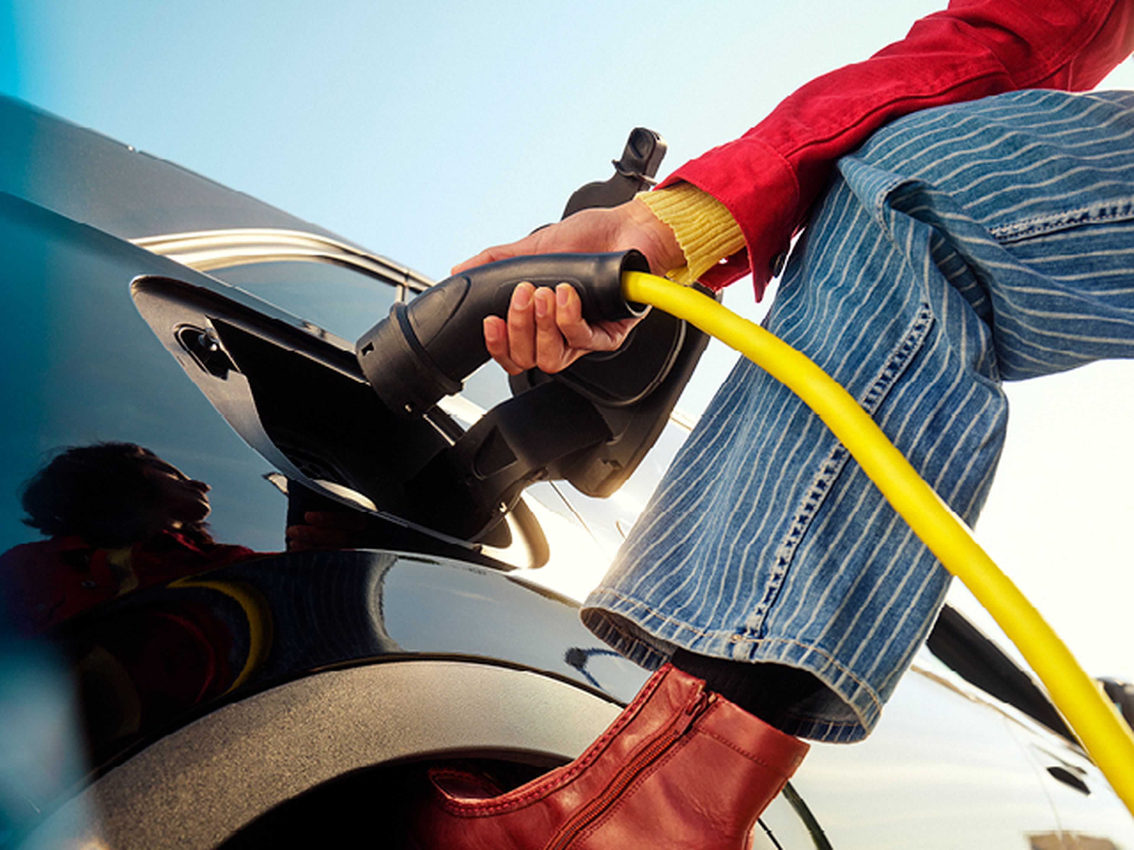Gros plan d’une personne branchant un câble de recharge jaune à une voiture électrique.