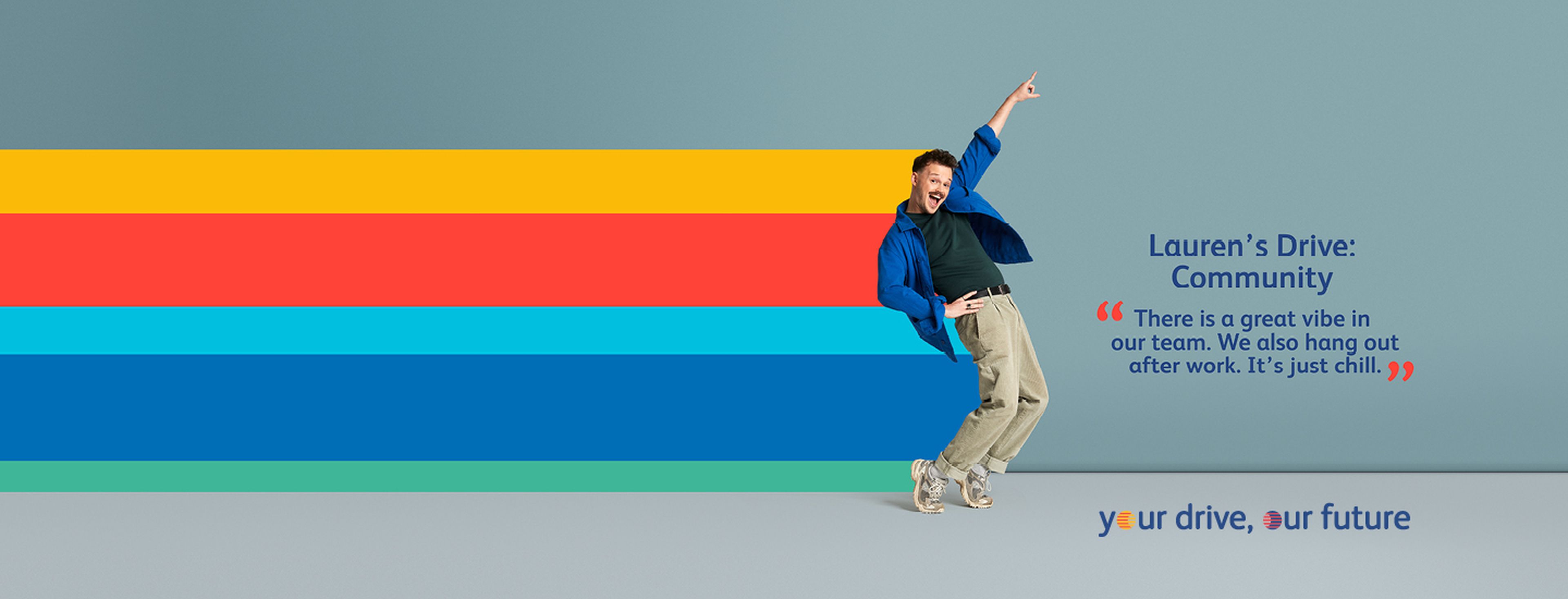 A boy with a mustache is standing on tiptoes and pointing upwards while smiling at the camera.