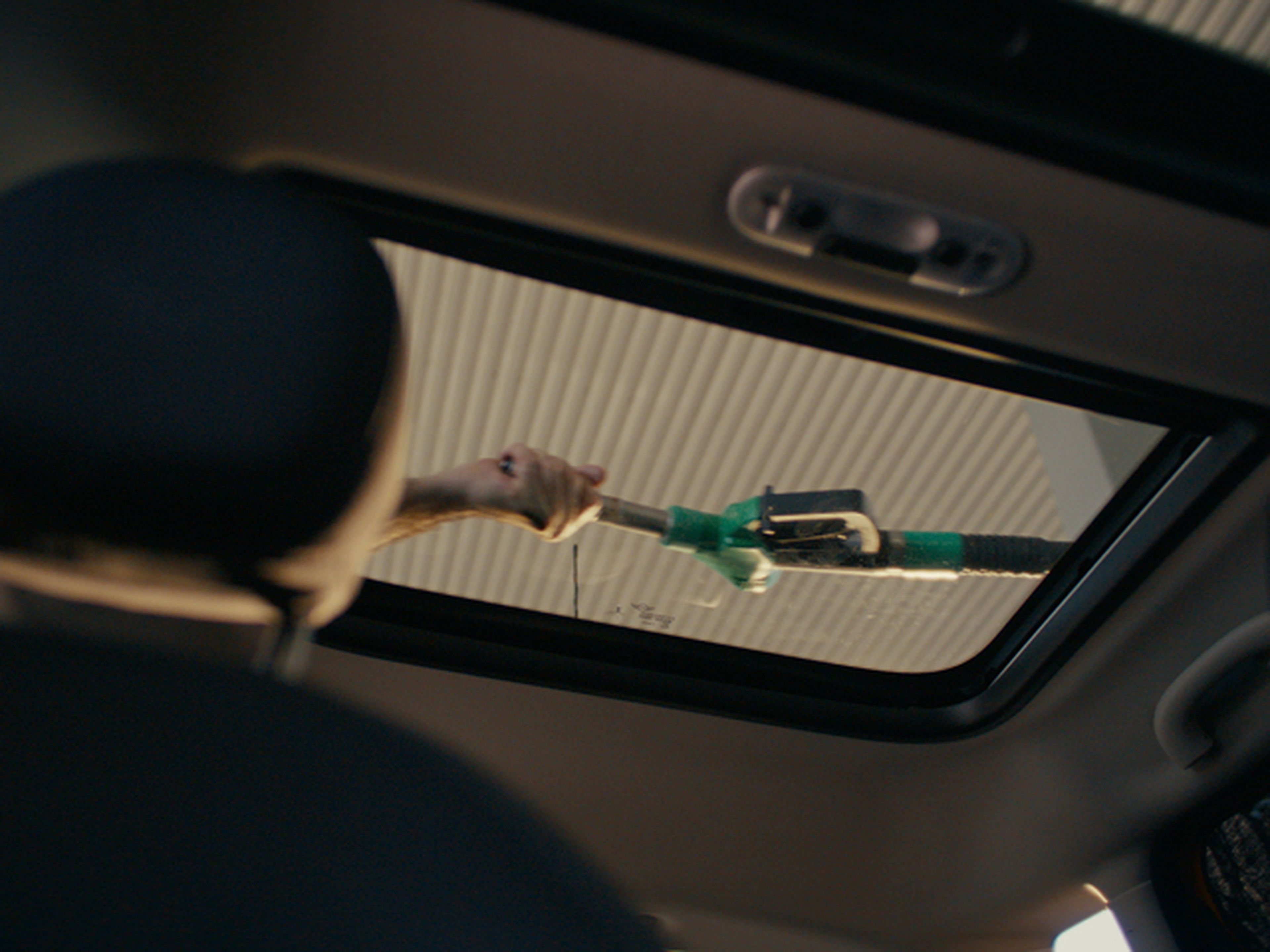View from inside car showing a man pulling the fuel pump nozzle over the vehicle to reach the fuel tank.