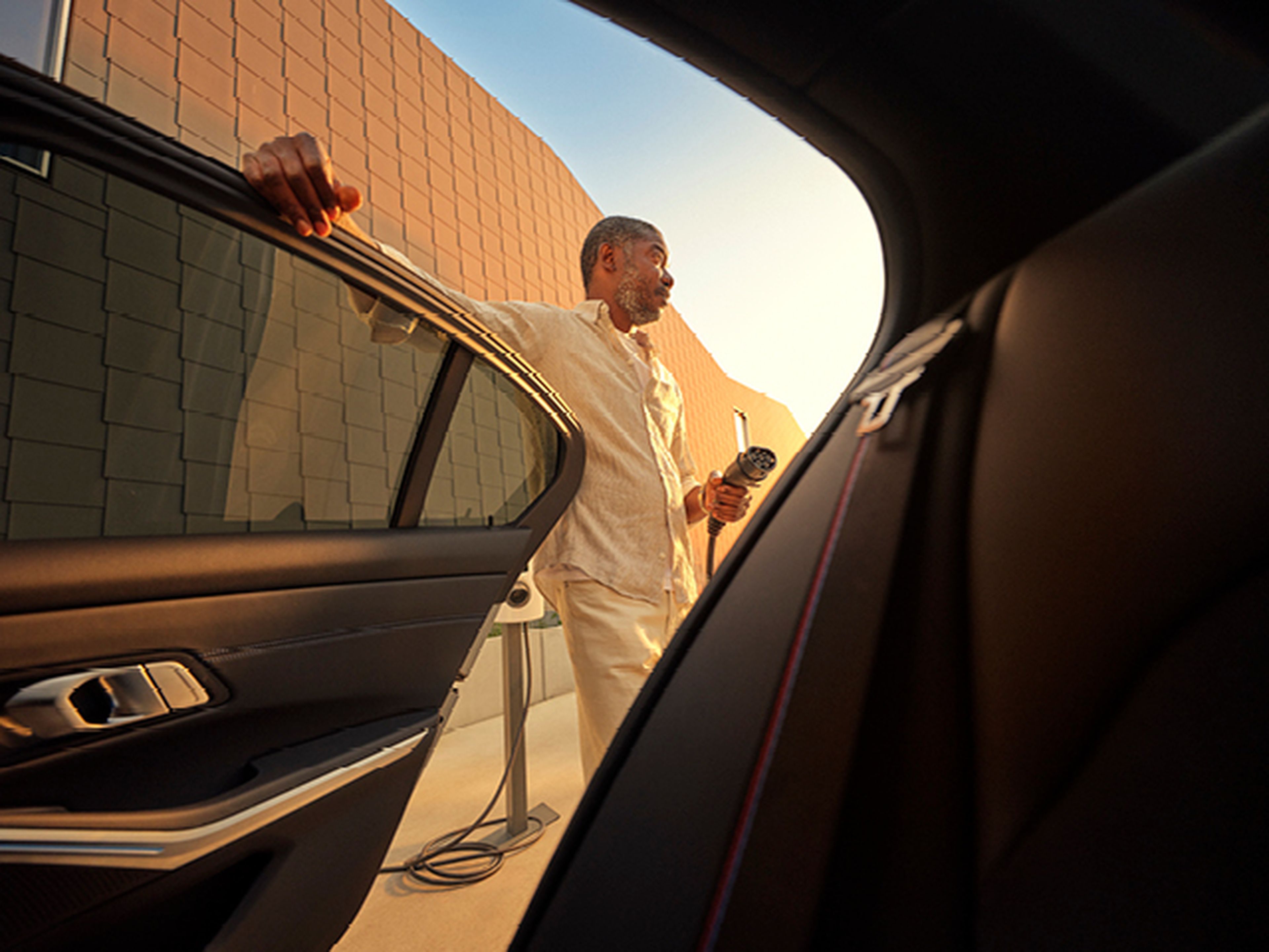 Homme avec câble de recharge près d'une voiture électrique, vu de l'intérieur, chez Q8.