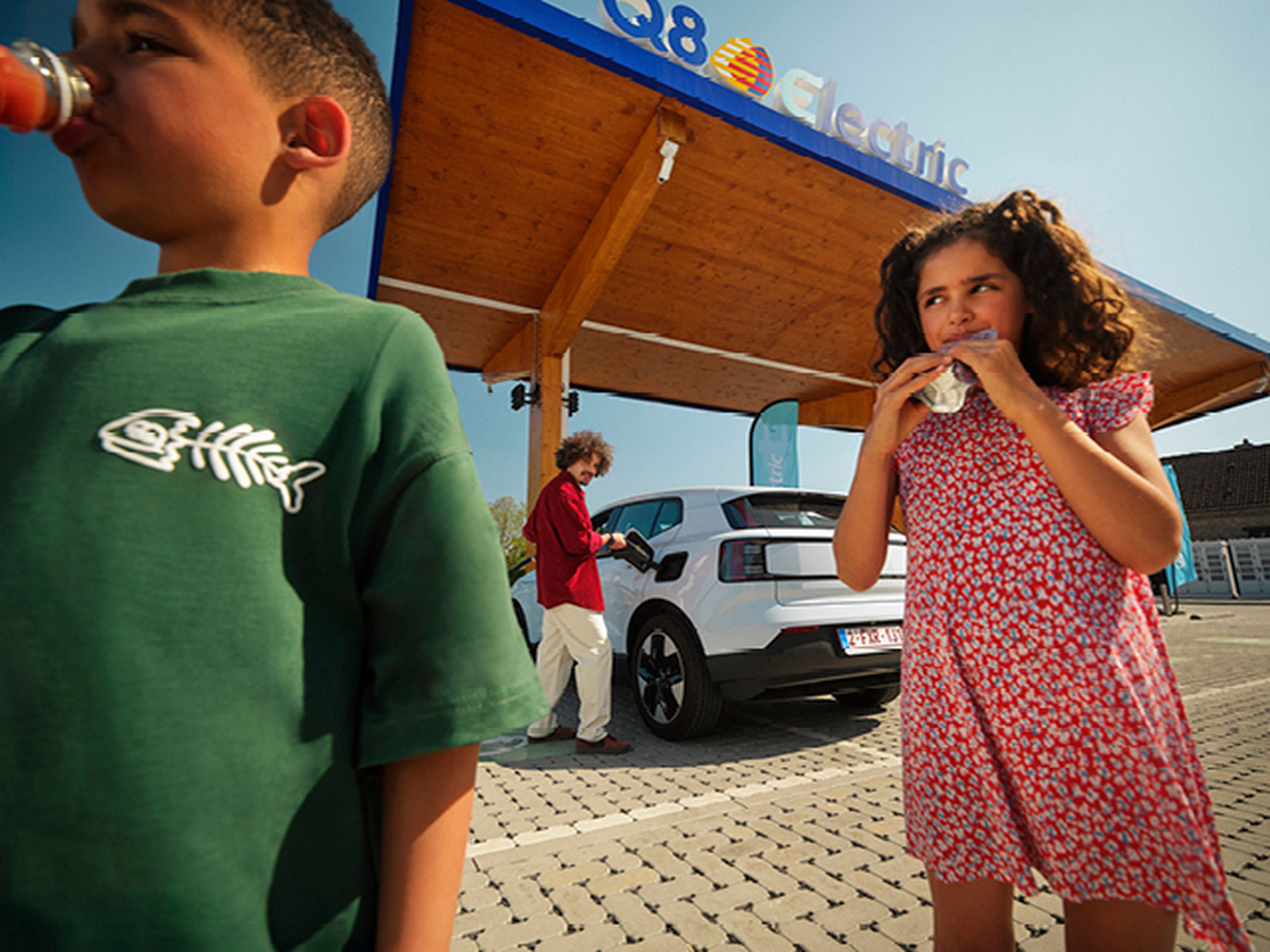 Kinderen drinken terwijl een man een elektrische auto laadt bij een Q8 Electric station.