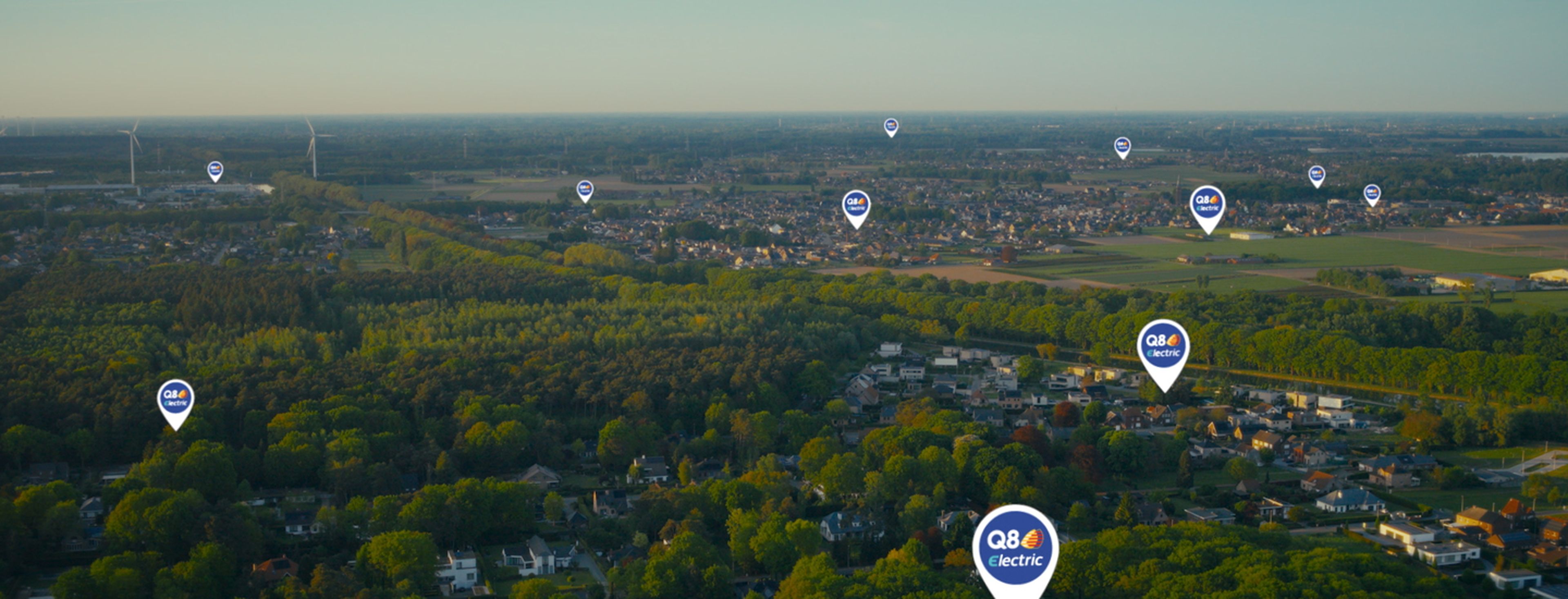 Luchtbeeld van een groene omgeving met woonwijken, windmolens en meerdere “Q8 electric”-locatiepinnen verspreid over het landschap, die laadpunten voor elektrische voertuigen aanduiden.