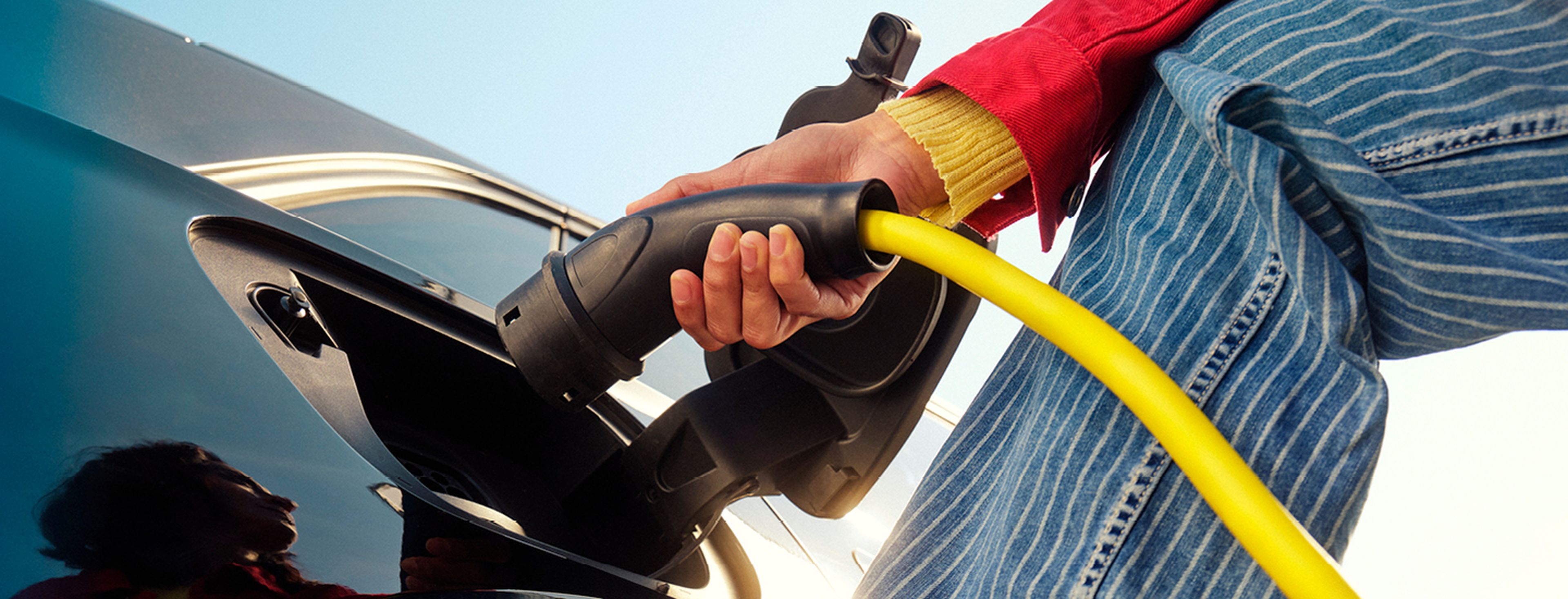 Femme recharge une voiture électrique avec un câble jaune chez Q8.