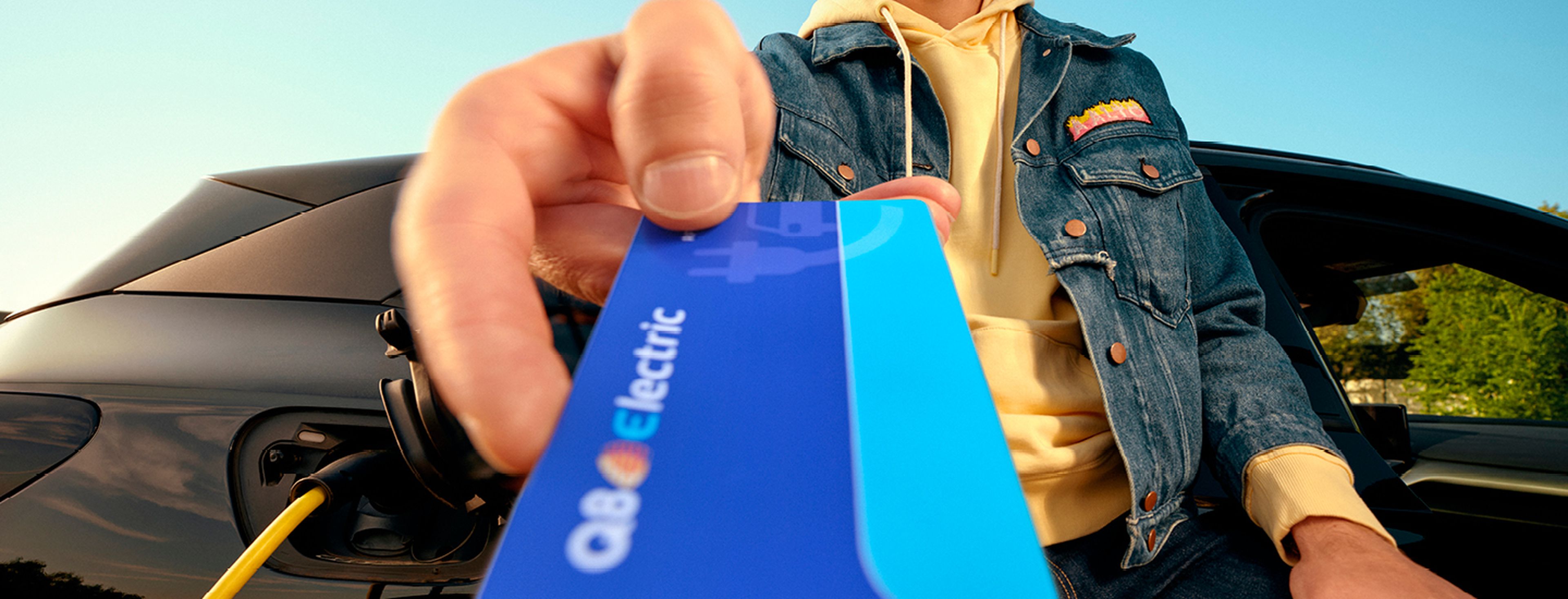 Homme montre une carte de recharge Q8 Electric près de sa voiture électrique chez Q8
