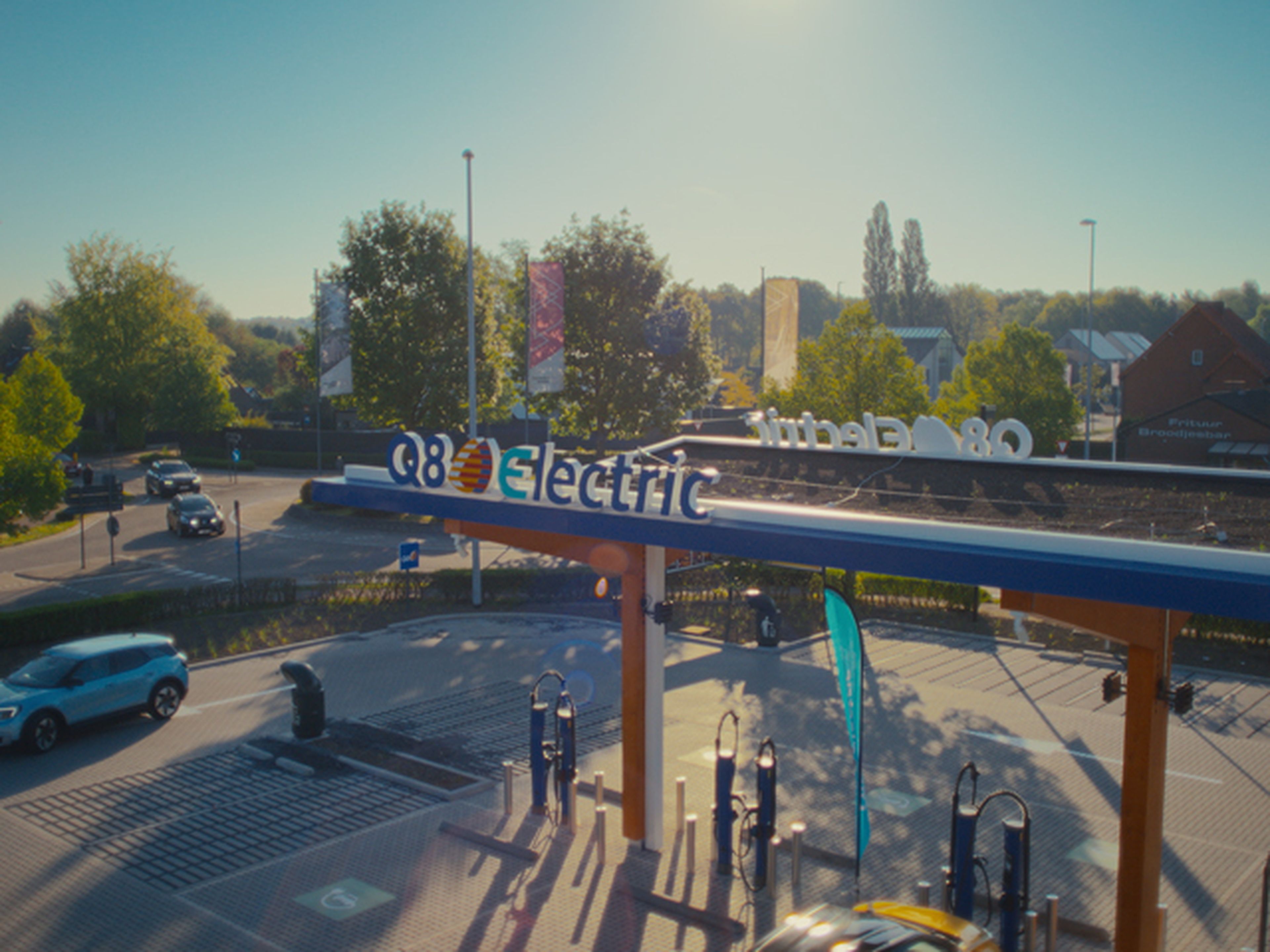 Luchtfoto van een Q8 electric snellaadstation omgeven door groen en bomen, met meerdere laadpunten onder een overkapping.