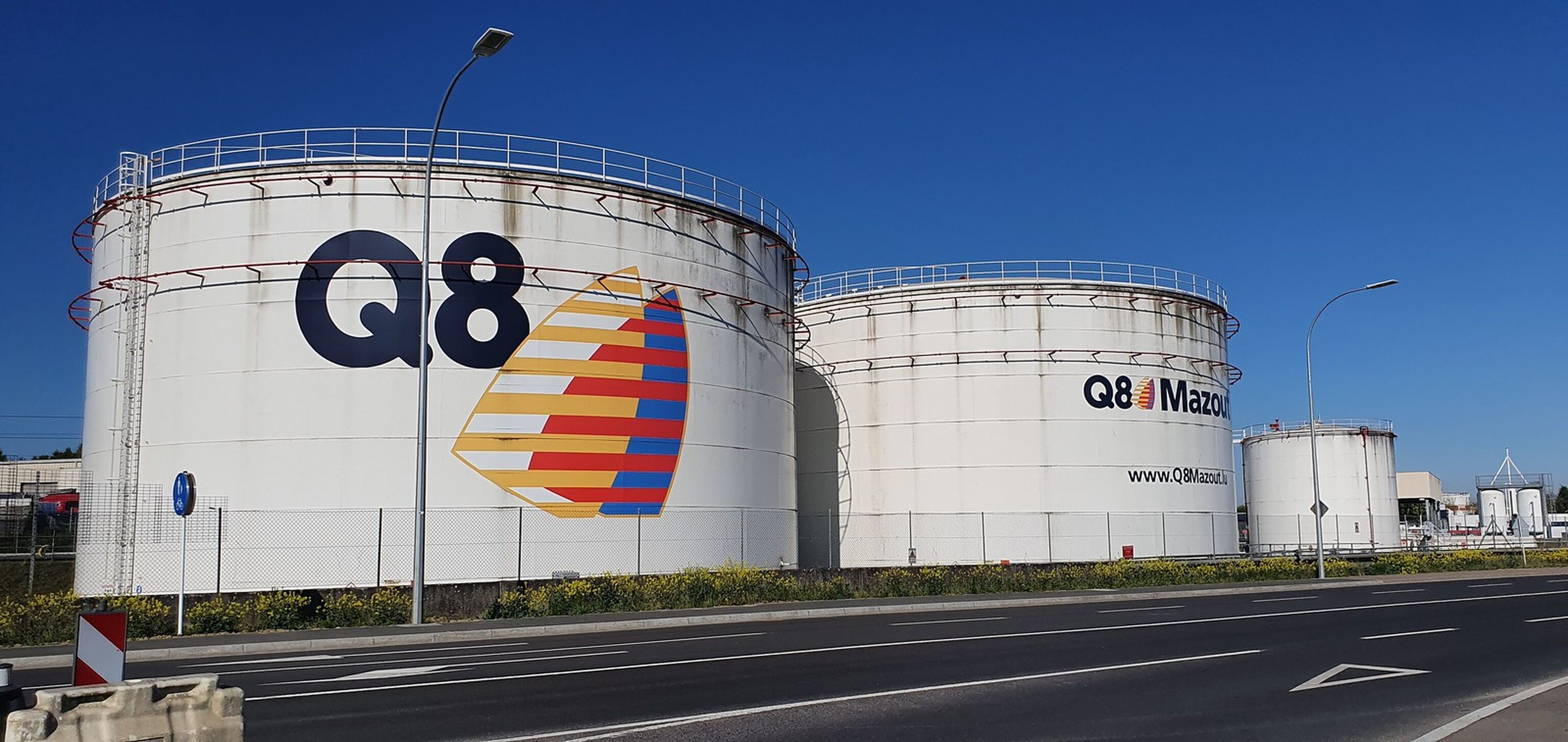 Three large white Q8 storage tanks along a road, with the Q8 logo on the left tank.