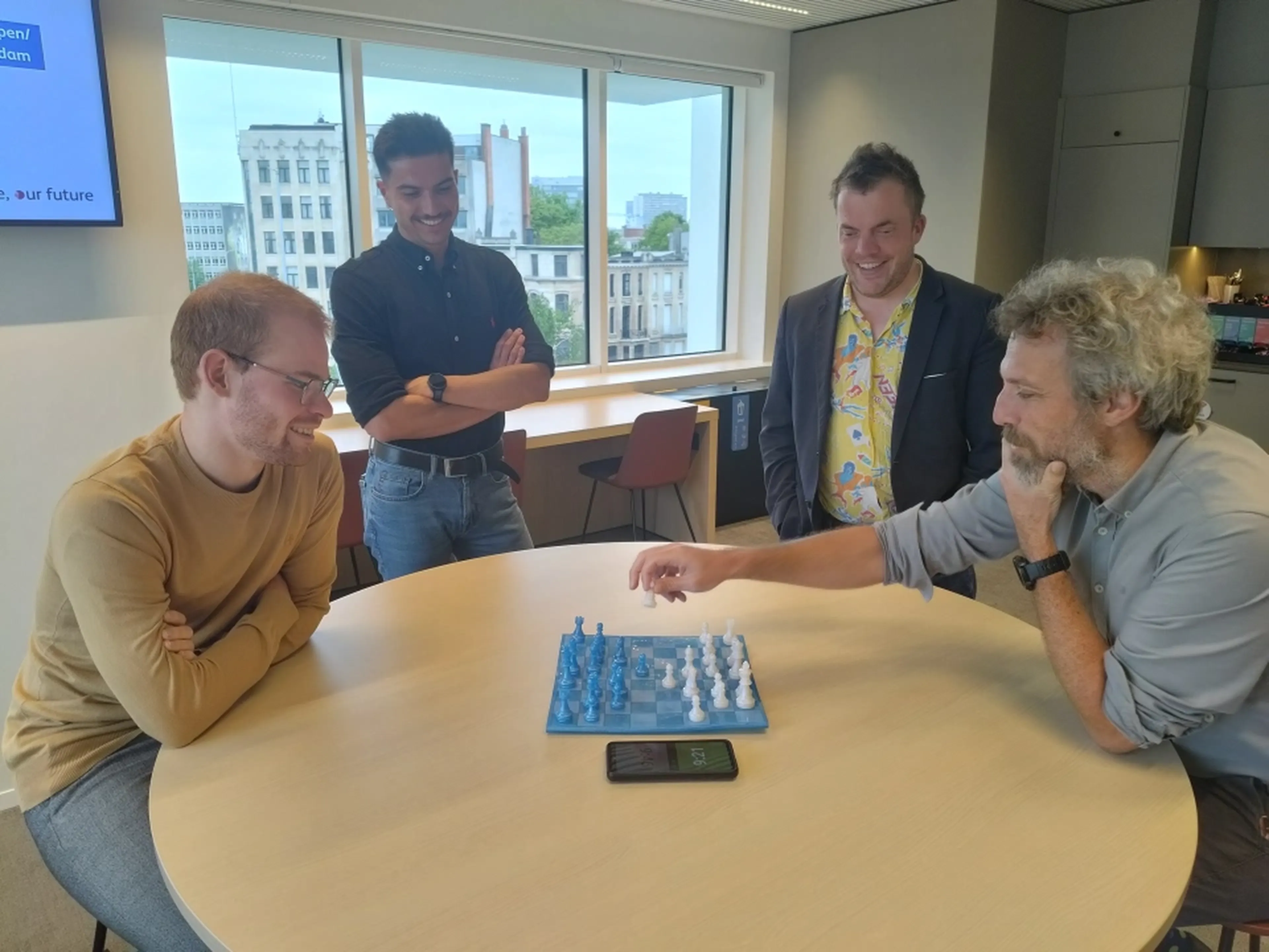 Two Q8 colleagues are playing a game of chess against each other while two other colleagues are watching.