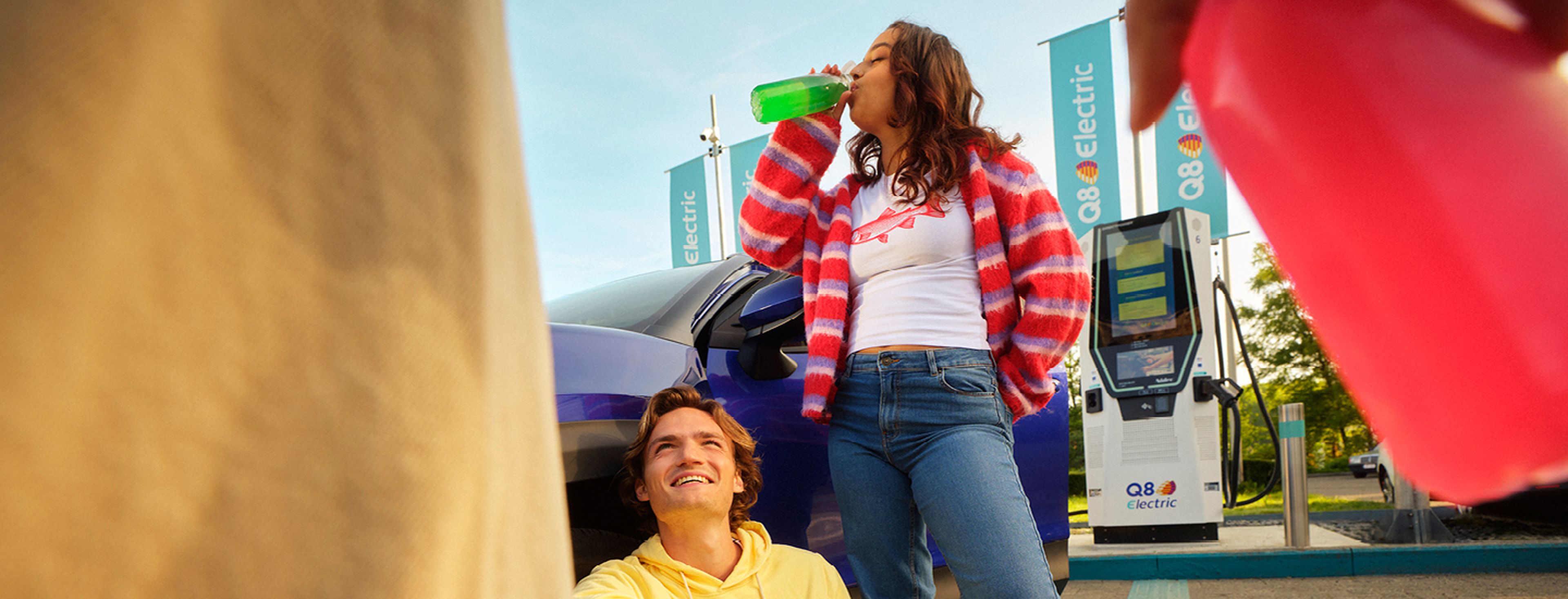 Young people drinking and relaxing at a Q8 Electric charging station.