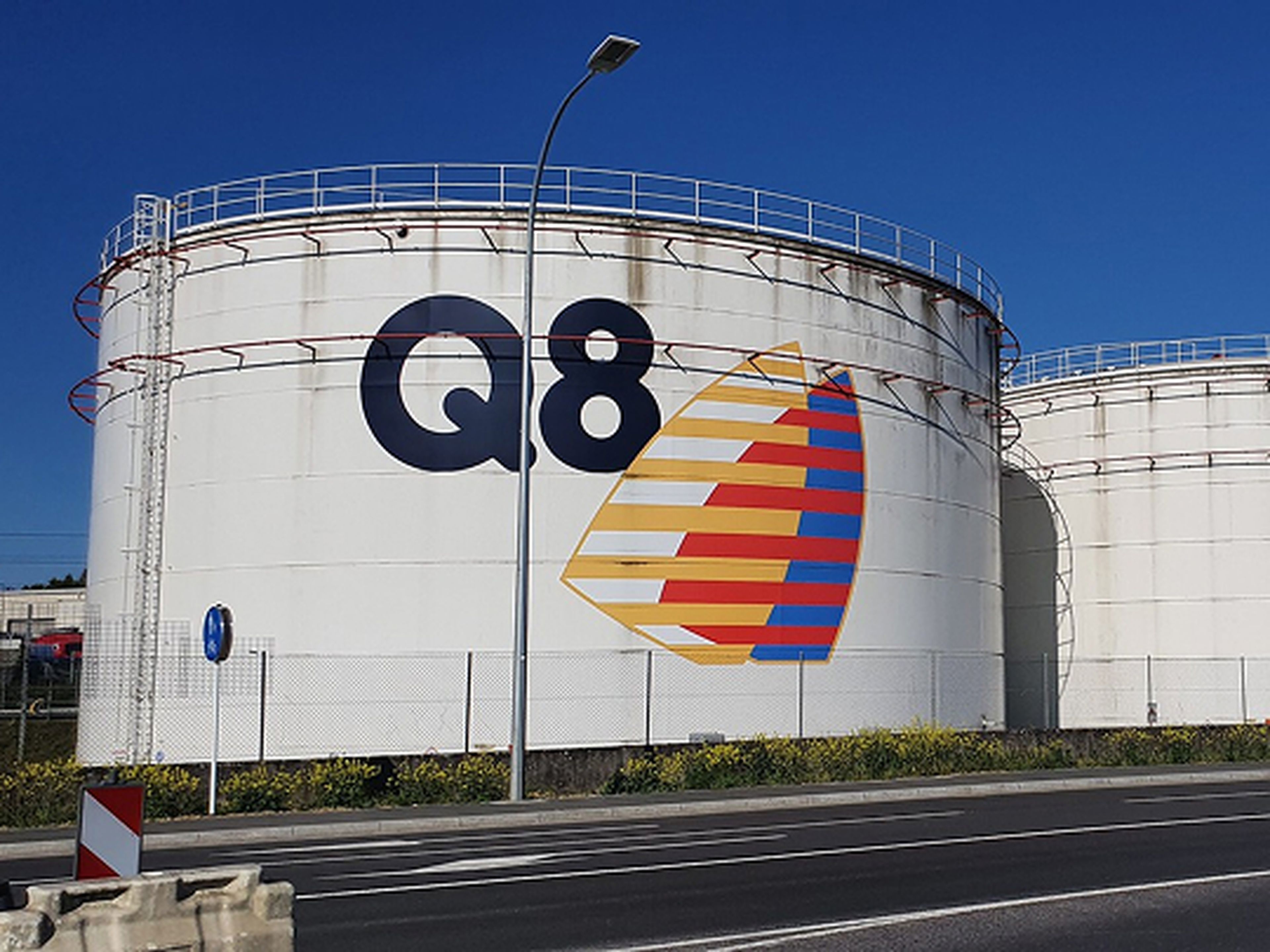 Drie grote witte opslagtanks van Q8 langs een weg, met het Q8-logo op de linkertank.