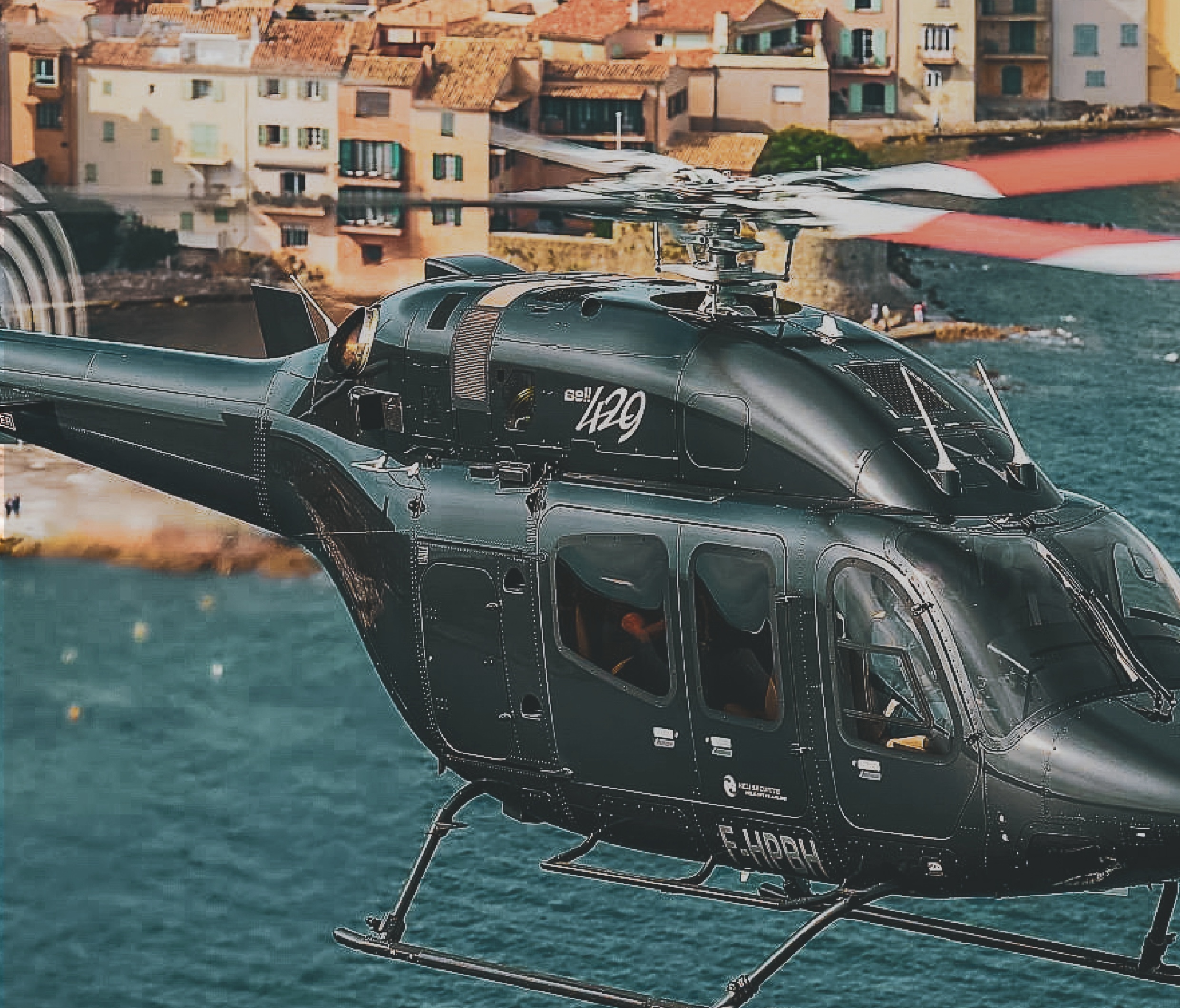 Black helicopter flying over turquoise water with colorful buildings in the background.