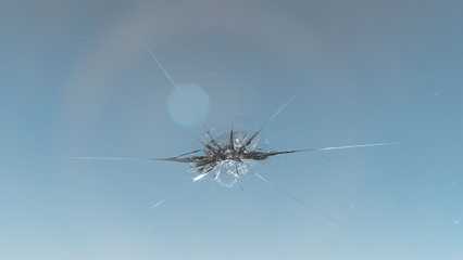 Close-up of a cracked windshield against a clear blue sky, showing a central impact point with radiating cracks.