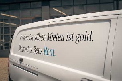 White Mercedes-Benz van with German text "Reden ist silber. Mieten ist gold. Mercedes-Benz Rent" on its side, parked outside a building.