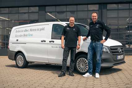 Two men standing in front of a white Mercedes-Benz van with rental service branding, parked on a paved area.