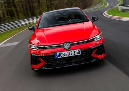Red Volkswagen Golf GTI driving on a winding road through a wooded area.
