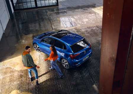 A man and woman walking near a parked blue car inside an industrial-style building with wet, textured flooring.