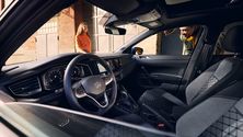 polo car interior showing modern dashboard and steering wheel, with two people outside, one peering through the driver's window, and one in the background.