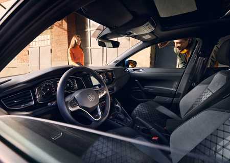 polo car interior showing modern dashboard and steering wheel, with two people outside, one peering through the driver's window, and one in the background.