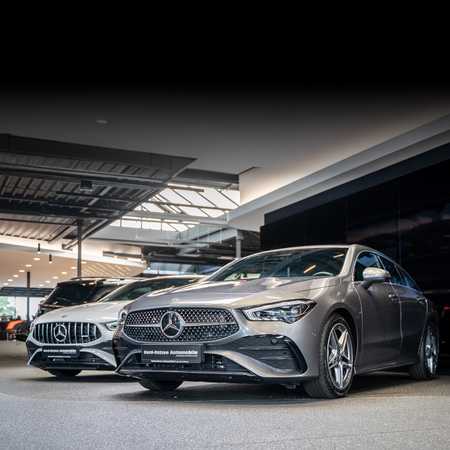 Two sleek Mercedes-Benz cars are displayed in a modern showroom with bright lighting and a polished floor.