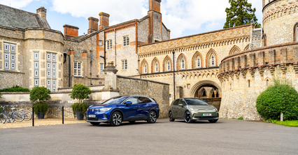 Two modern SUVs parked in front of a historic stone building with large windows and arches on a clear day.