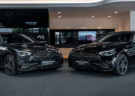 Two sleek black Mercedes-Benz cars are displayed in a modern showroom with bright lighting and a glossy floor.