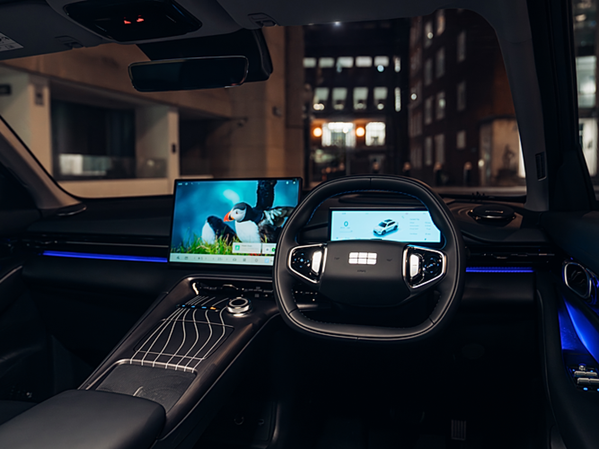 Futuristic car interior with digital display screens, modern steering wheel, and ambient blue lighting, parked at night in an urban setting.