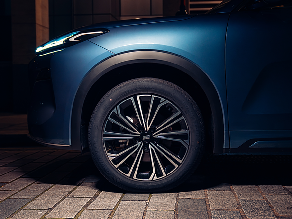 Close-up of a blue car's front wheel and fender, illuminated at night, parked on a cobblestone street.