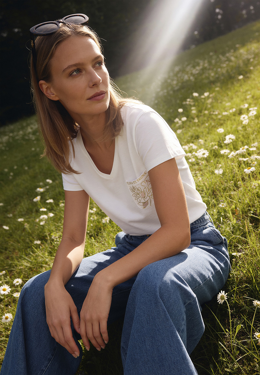 Model in weiter Jeanshose und weißem Shirt sitzend in einer Wiese