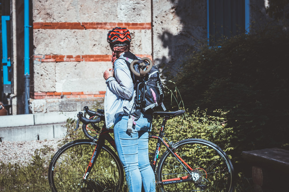 Frau steht mit dem Rennrad in Jeans vor einem Gebäude auf dem Weg zur Arbeit.