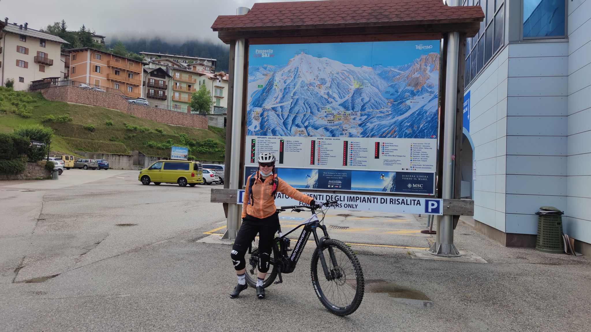 Lisa steht mit dem E-Bike vor einer Bergkarte an der Talstation in Paganella.