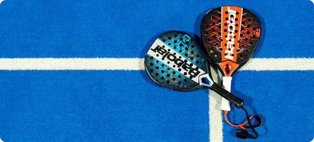 Two padel rackets, one black and blue, the other black and orange, rest on a blue court with white lines, illustrating a visual guide on how to choose a padel racket, serving as a helpful padel racket guide.
