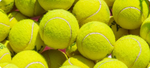 A pile of bright yellow tennis balls is shown, illustrating the difference between padel and tennis balls.