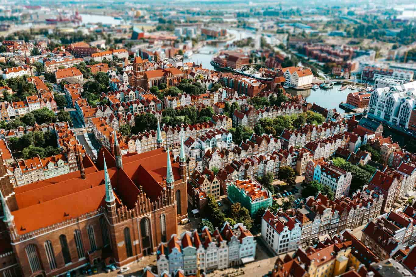 Aerial view of a European city with red-roofed buildings, historic architecture, and a winding river surrounded by green trees.