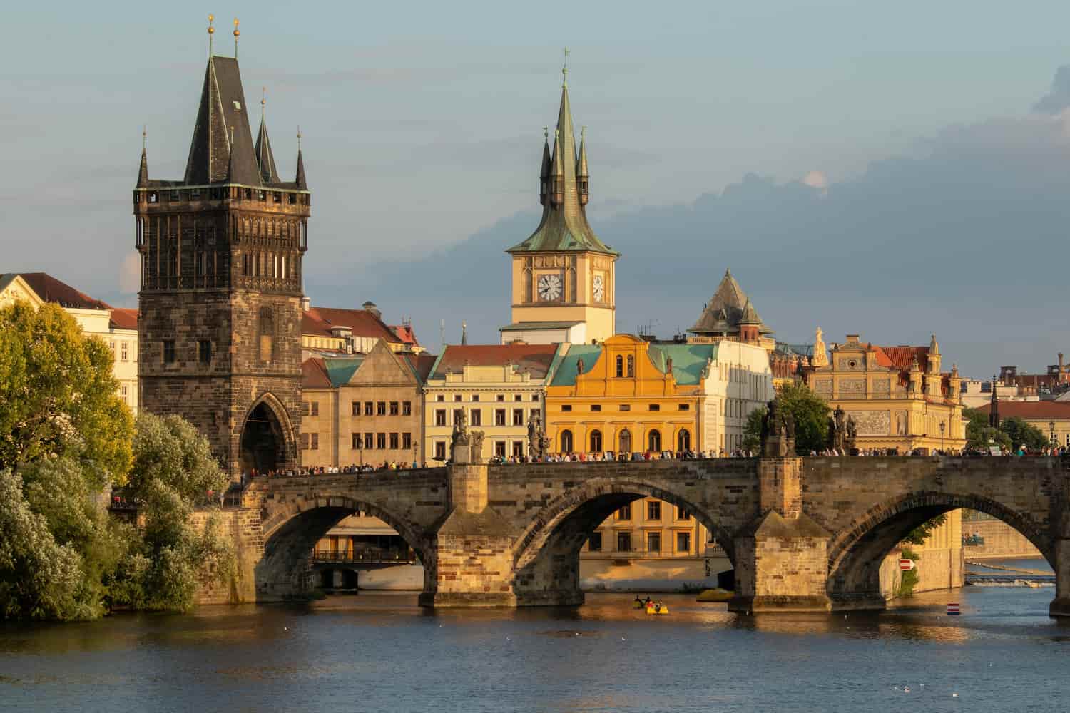 Historic stone bridge over a river with buildings and clock towers in the background under a clear sky.