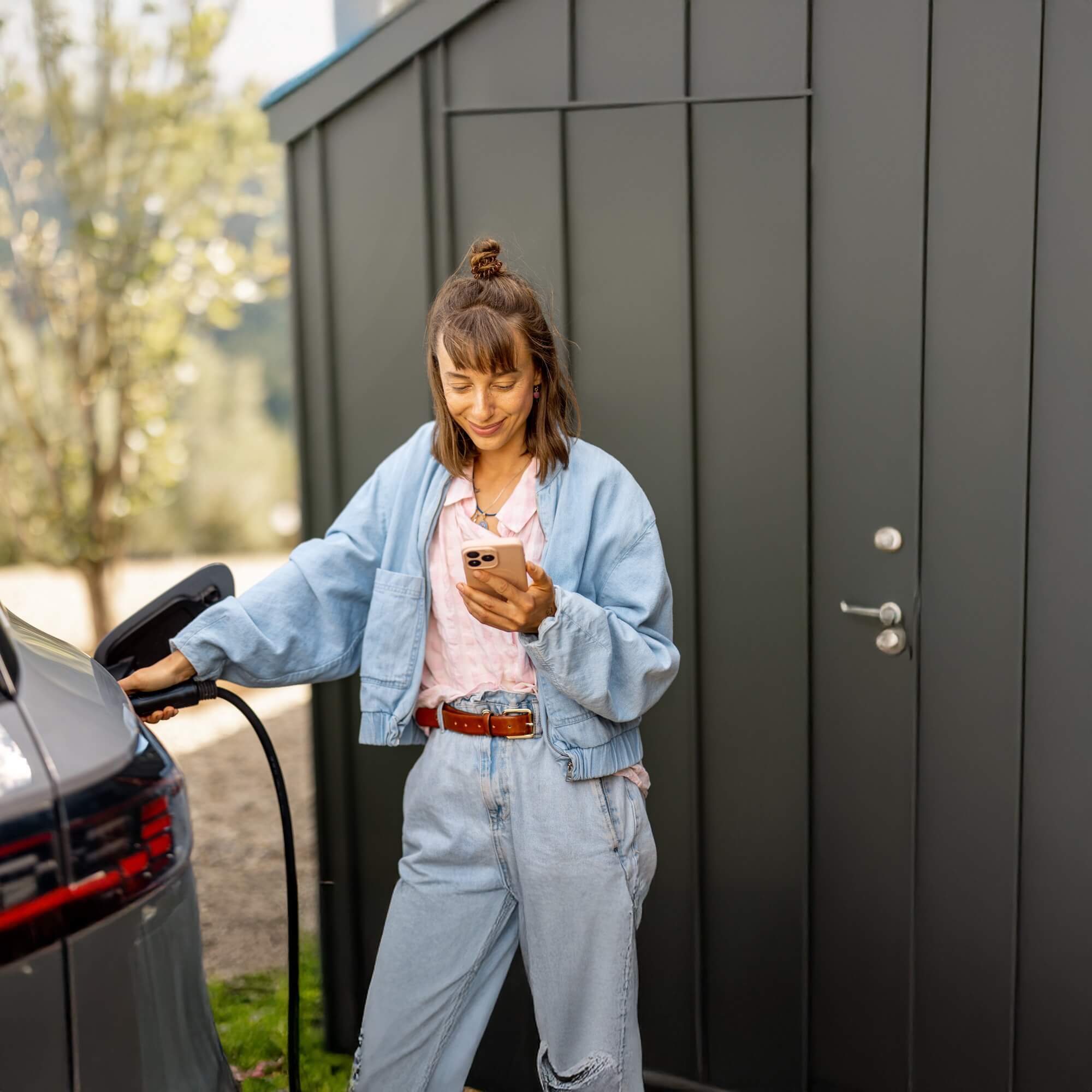 Frau lädt Elektroauto und blickt dabei auf ihr Smartphone