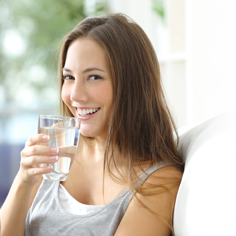 Frau mit Wasserglas in der Hand lacht freundlich in die Kamera