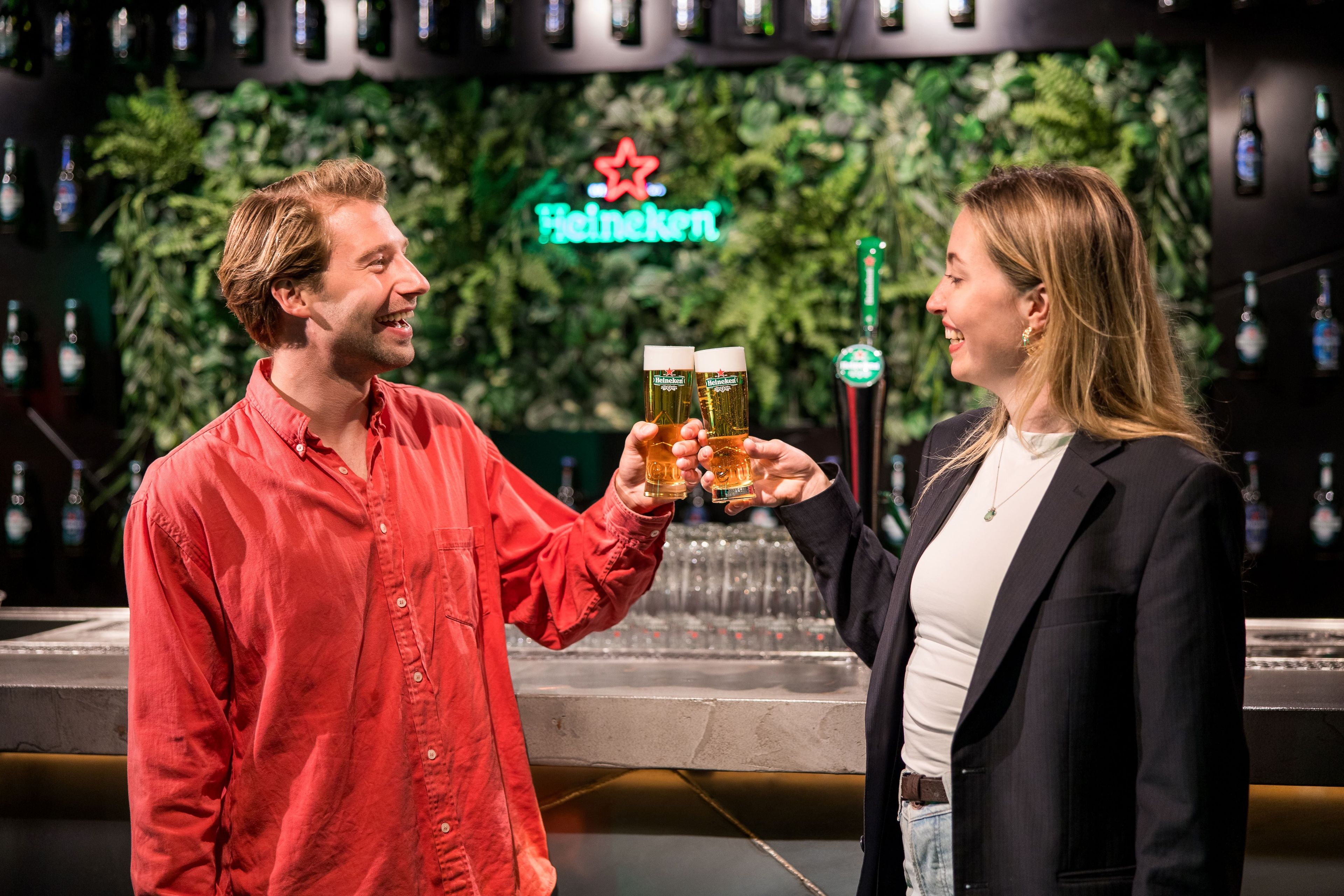 Two people toasting with glasses of beer in a Heineken bar setting.