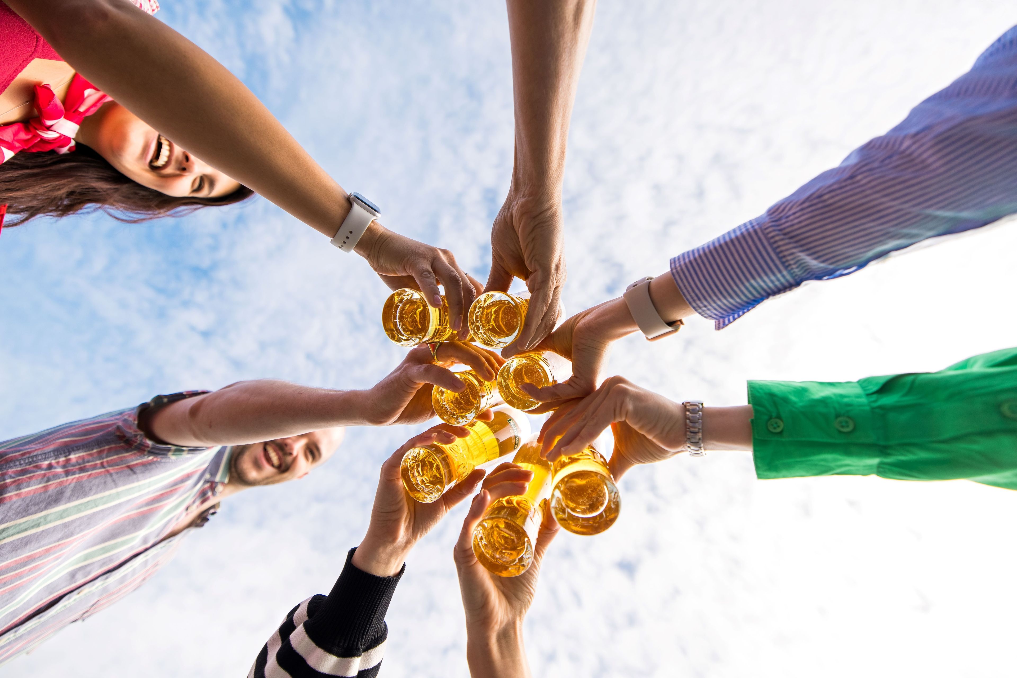 A group of people toasting with glasses of beer against a blue sky.