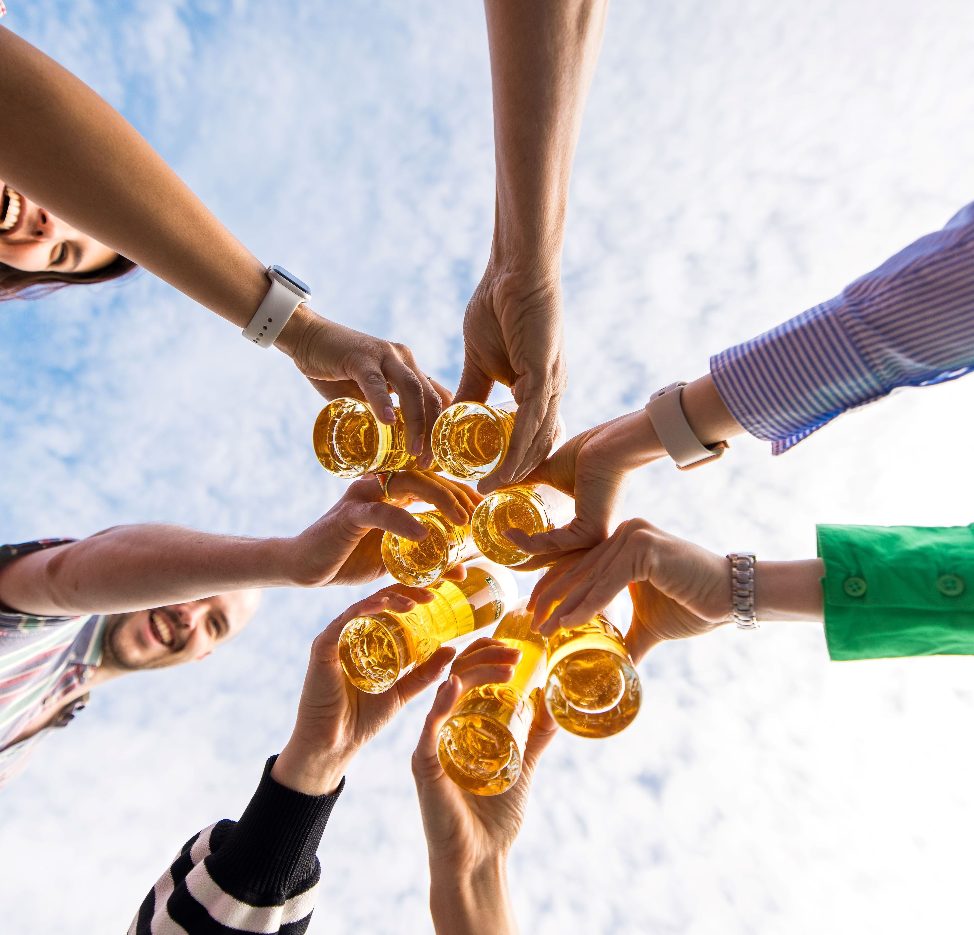 A group of people toasting with glasses of beer against a blue sky.