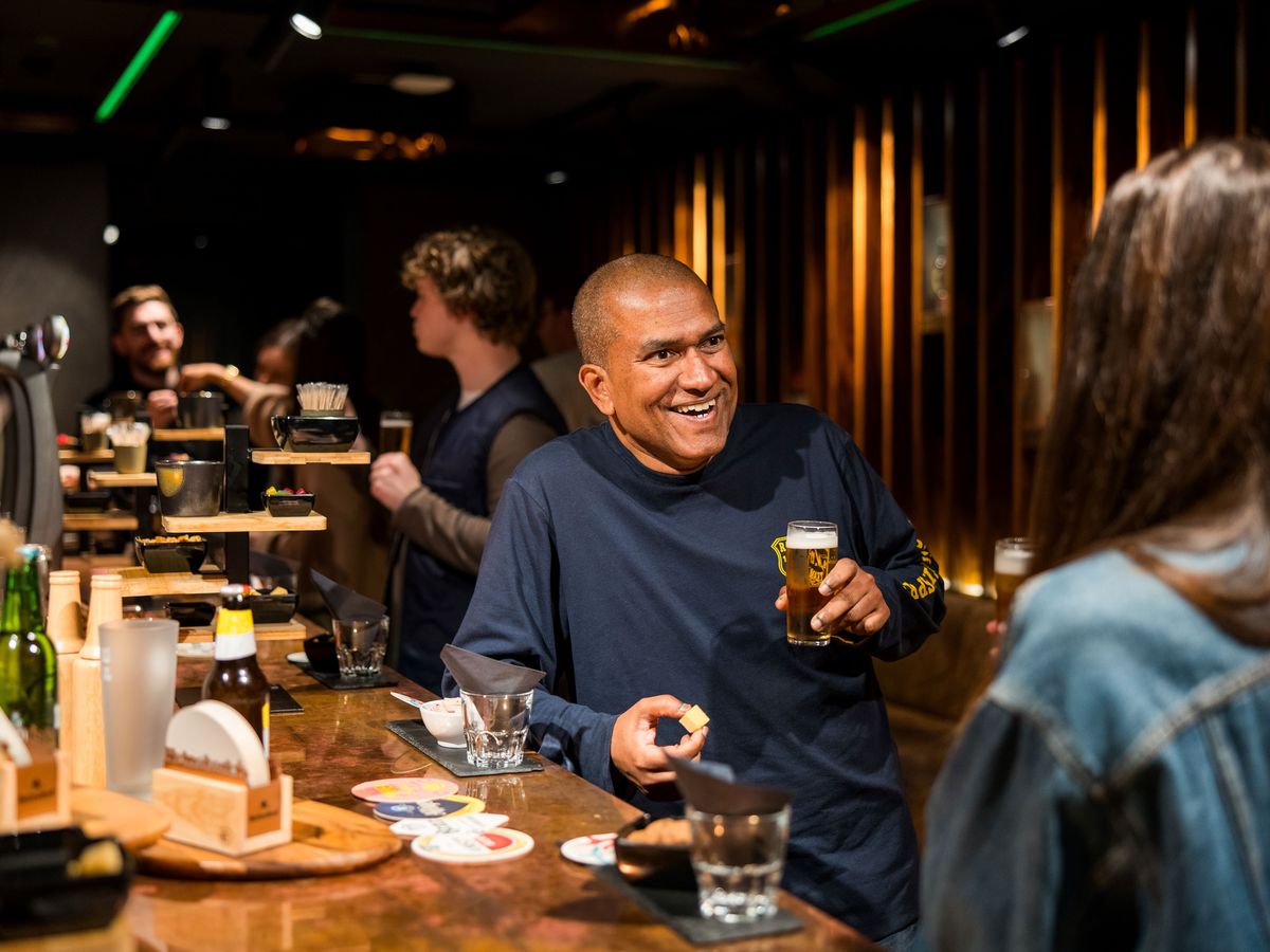 A man smiling and holding a beer while interacting with others at a bar