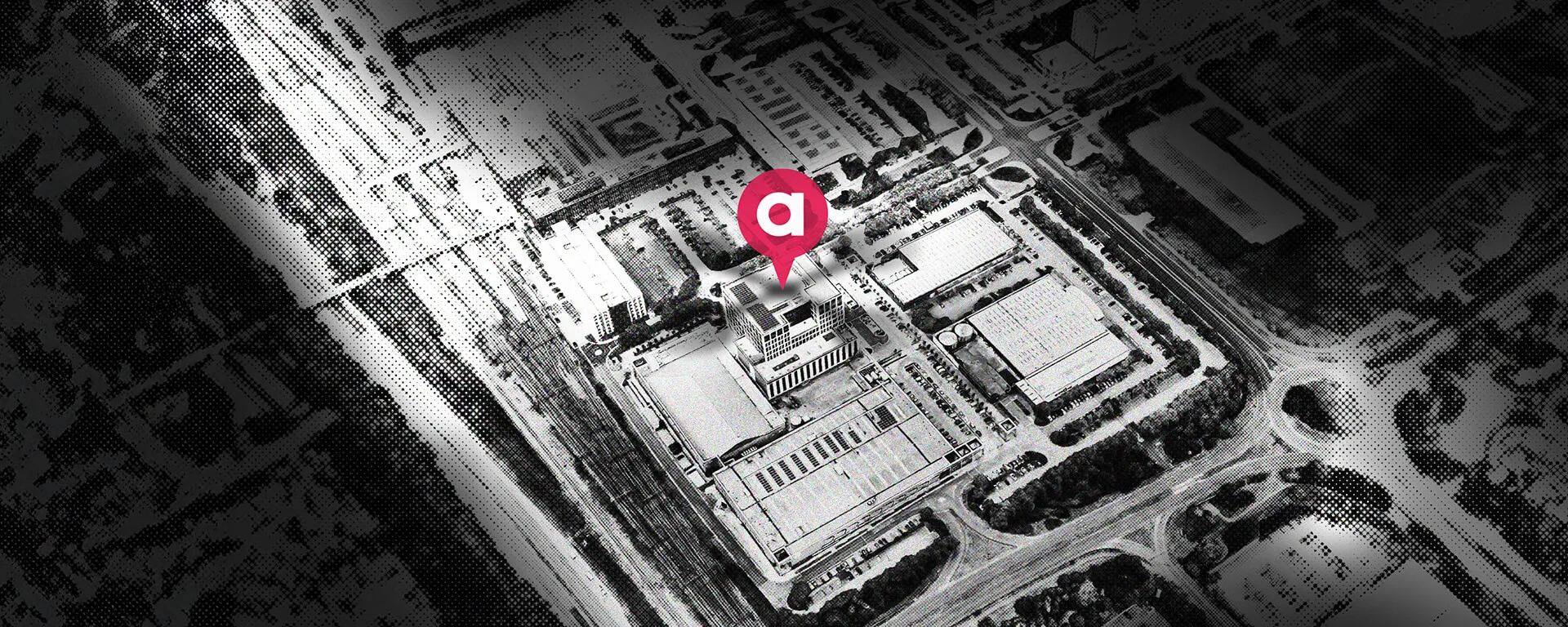 Aerial view of a city block with a location pin marking a specific building, surrounded by roads and other structures. Black and white filter.
