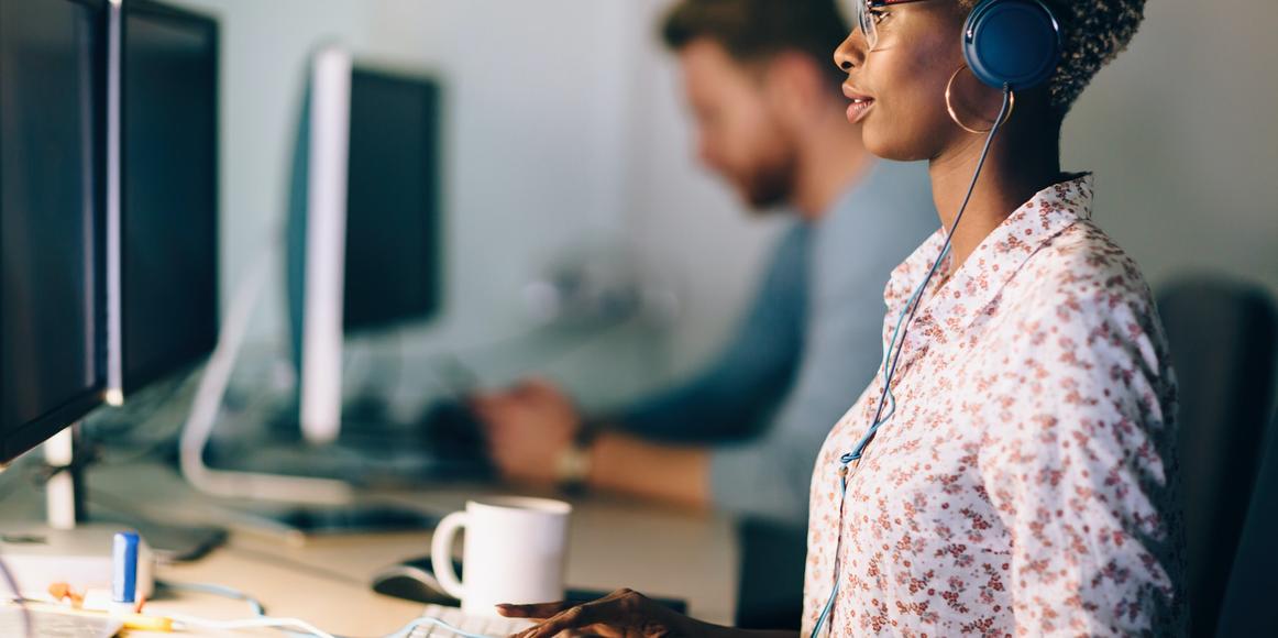 A person working at a desk, in front of a double-screen desktop computer.