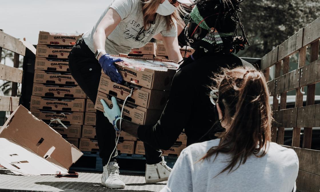 A volunteer is standing on the back of a truck, passing boxes of strawberries to other people.